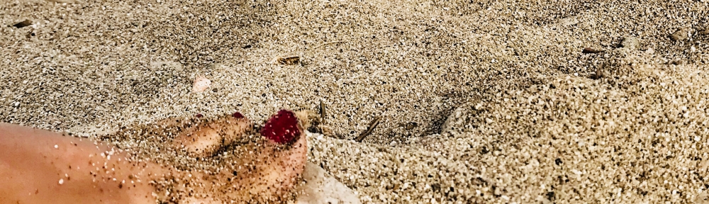 Dedo con uña roja sobre la arena de playa